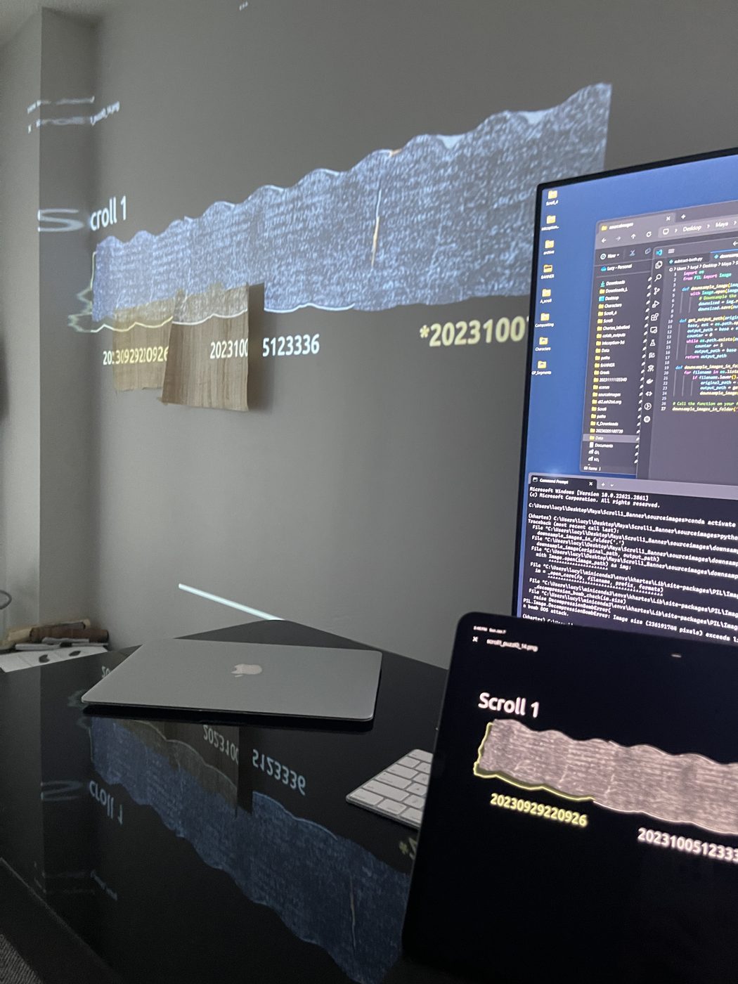 A segment of Scroll 1 projected large across a wall, next to monitors of code