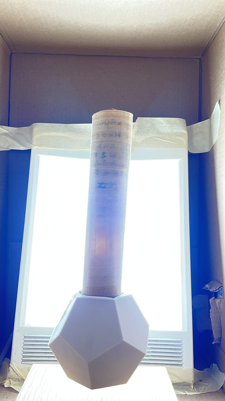 The rolled scroll standing in the light box, glowing